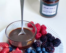 Load image into Gallery viewer, Portion of chocolate sauce with berries and a jar of Portland Caramel Co. chocolate caramel sauce on a white plate.