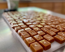 Load image into Gallery viewer, Caramel candies cut and ready to be hand wrapped in parchment paper, on cutting board.
