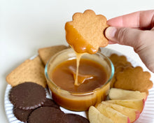Load image into Gallery viewer, Hand dipping a cookie into a bowl of caramel with more cookies on a plate
