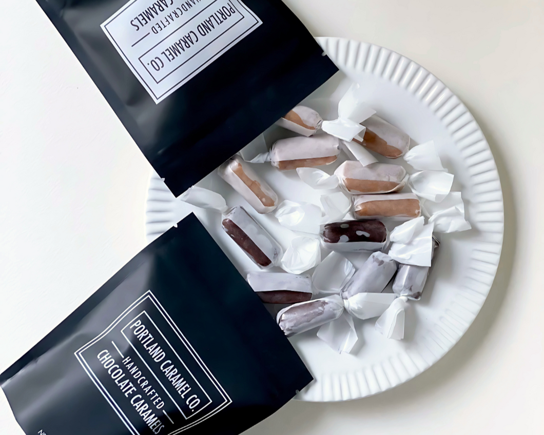 Two open black bags of Portland Caramel Co. chocolate caramels on a white plate with more caramels.